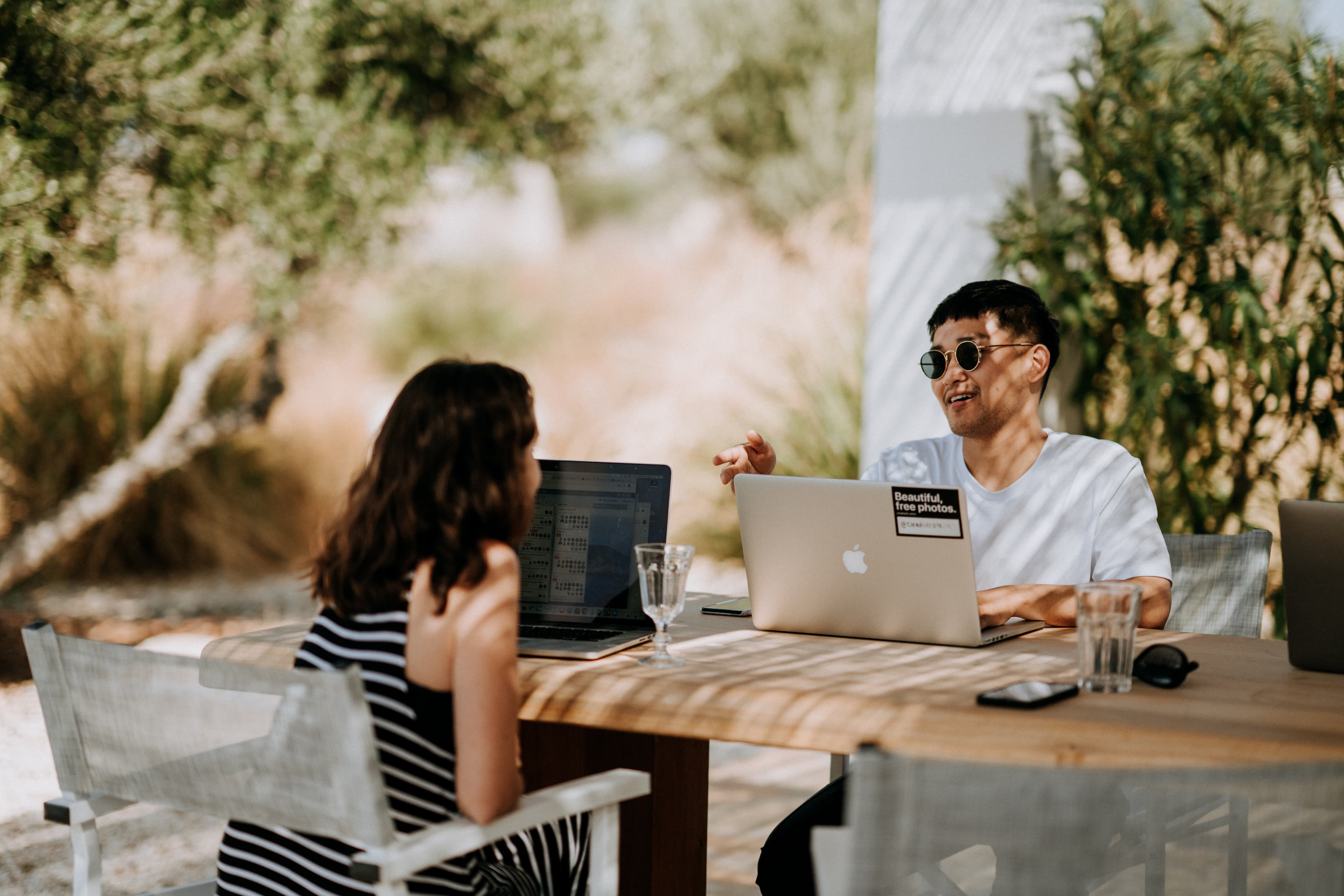Two people sitting outdoors using laptops and reviewing information together